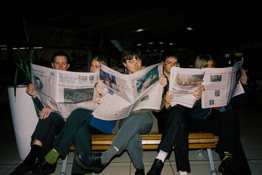 Aussie rock band Delivery sits in a row, reading newspapers